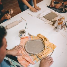 Zbliżenie na stół i dłonie uczestników wykonujących swoje ceramiczne prace.