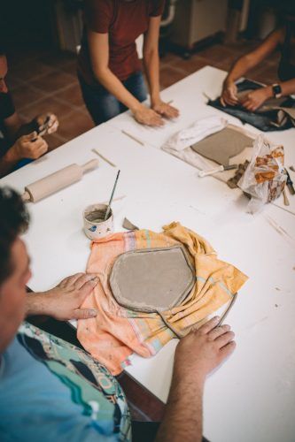 Zbliżenie na stół i dłonie uczestników wykonujących swoje ceramiczne prace.