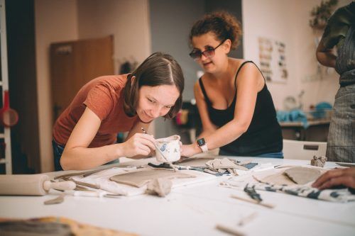 Na zdjęciu zrobionym w pracowni ceramicznej widać dwie dziewczyny, które ozdabiają farbami swoje prace.