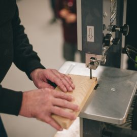 Zbliżenie na ręce osoby, który przy pomocy maszyny do cięcia drewna wycina pożądany kształt w kawałku grubszej listewki.