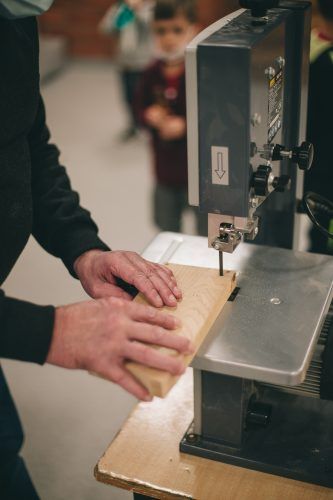 Zbliżenie na ręce osoby, który przy pomocy maszyny do cięcia drewna wycina pożądany kształt w kawałku grubszej listewki.